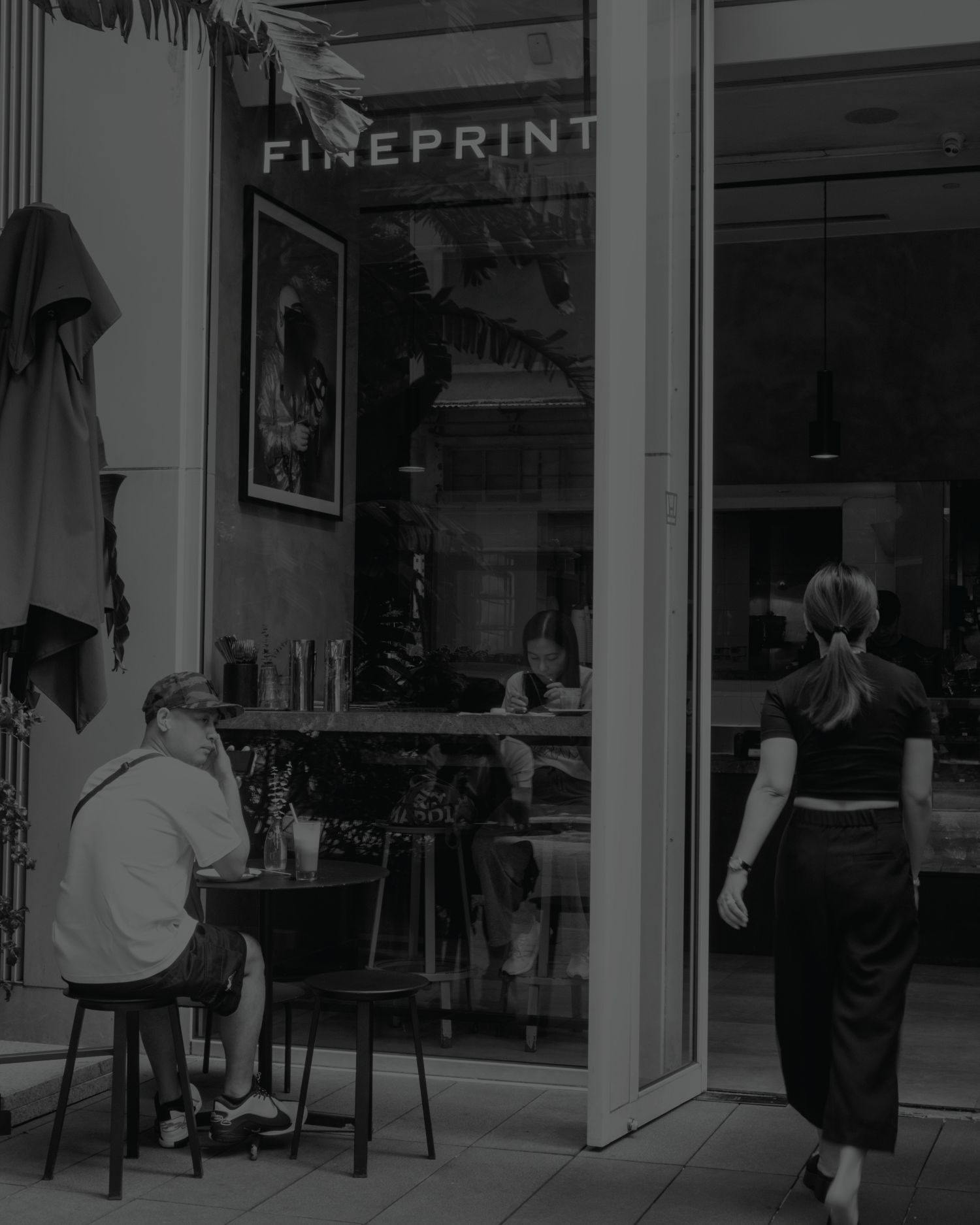 Monochrome photograph of FINEPRINT South Lane’s glass storefront, with its name above seated customers and a person entering.