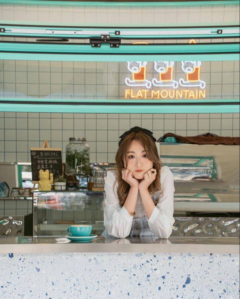 Flat Mountain Cafe’s open turquoise window and tiled coffee counter, with illuminated café lettering and a patron seated at the window.