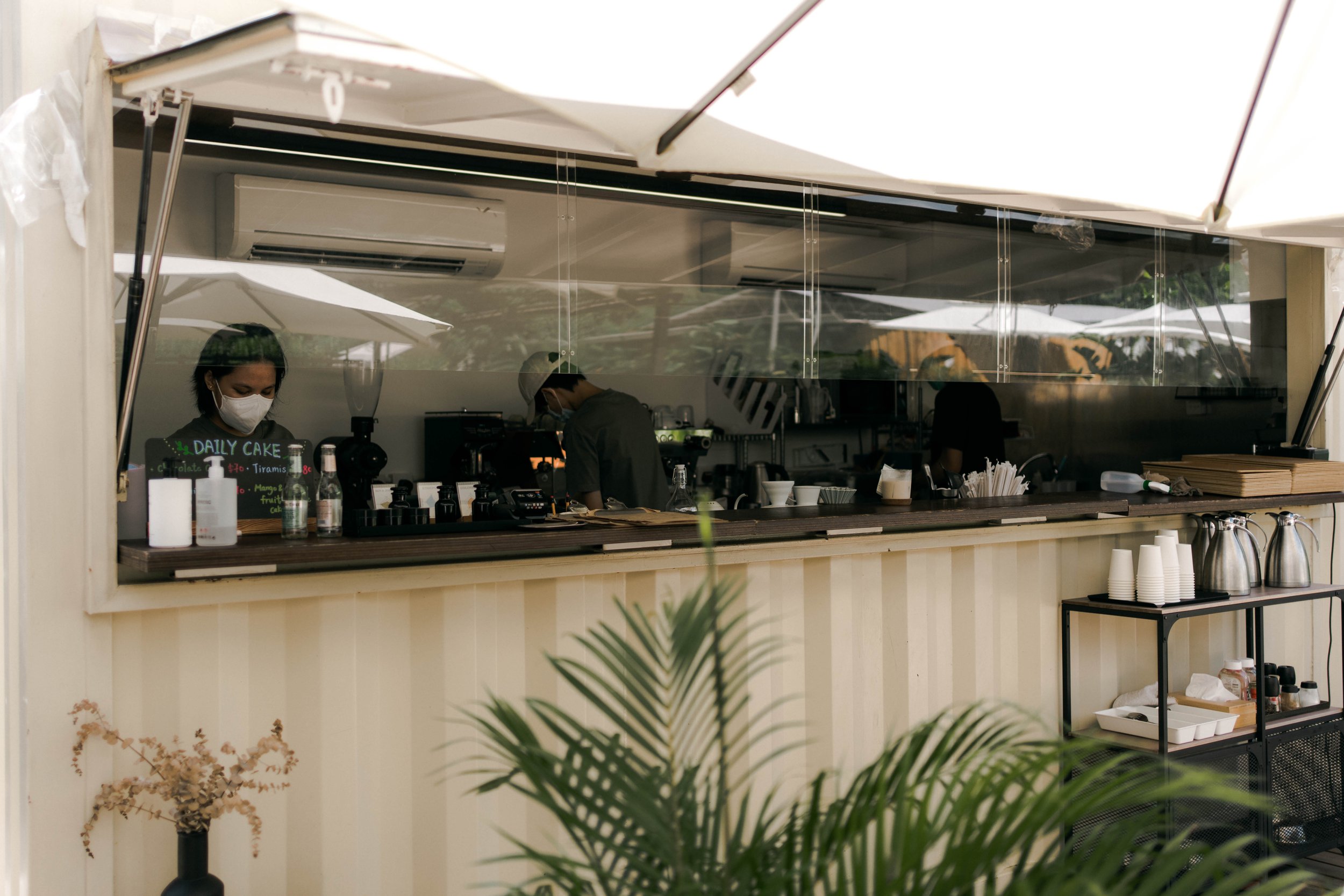 Staff prepare coffee behind The Hideout’s open serving counter beneath white umbrellas in Mui Wo.