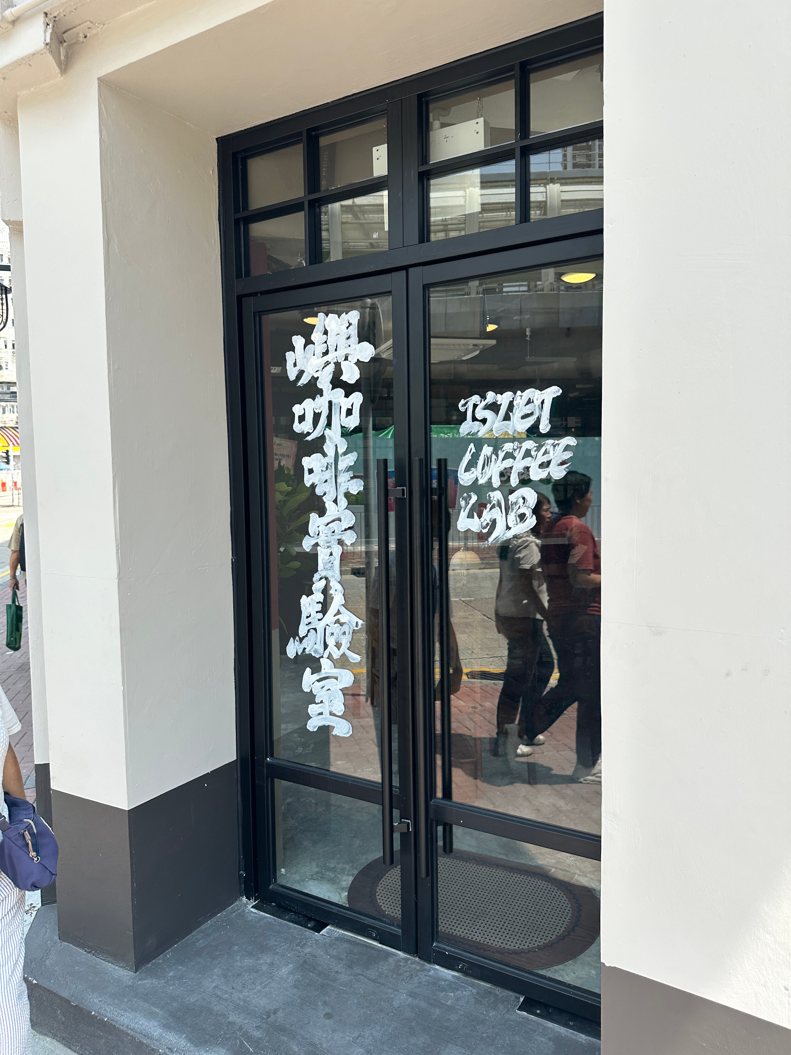 Glass storefront of Islet Coffee Lab’s Yau Ma Tei branch, with white Islet Coffee Lab lettering and cream exterior walls.