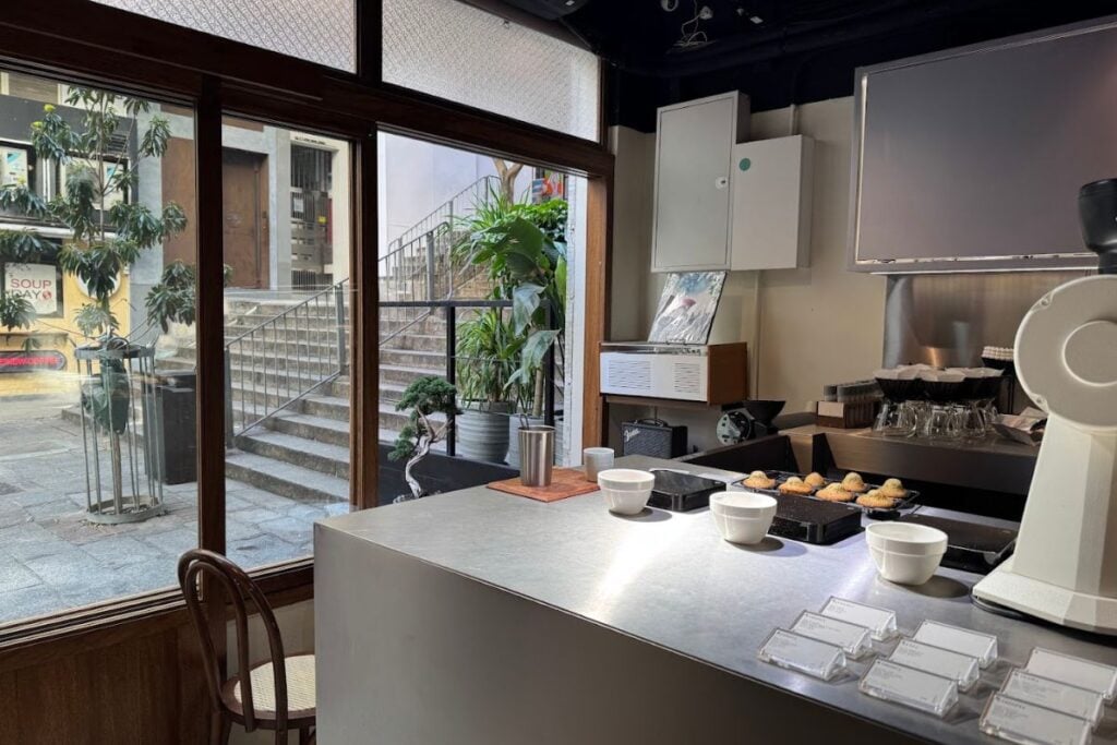 E N’s stainless-steel coffee counter beside windows overlooking the steps of Shin Hing Street.