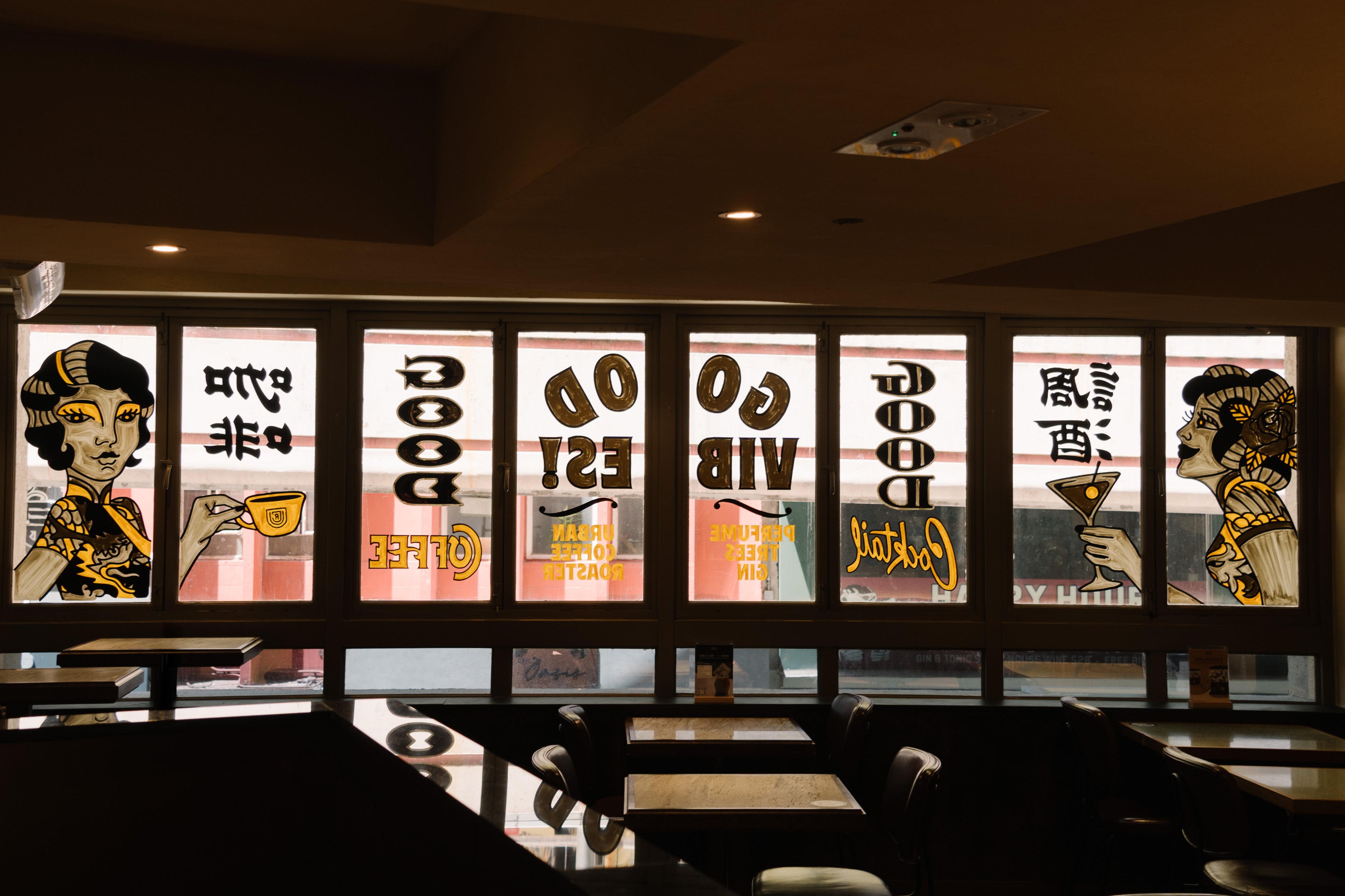 Window-side tables and illustrated glass panels inside Urban Coffee Roaster on Hollywood Road.