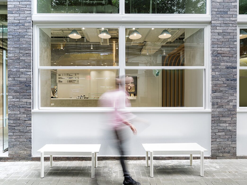 NOC Tin Hau white-framed storefront, outdoor benches and a passing pedestrian