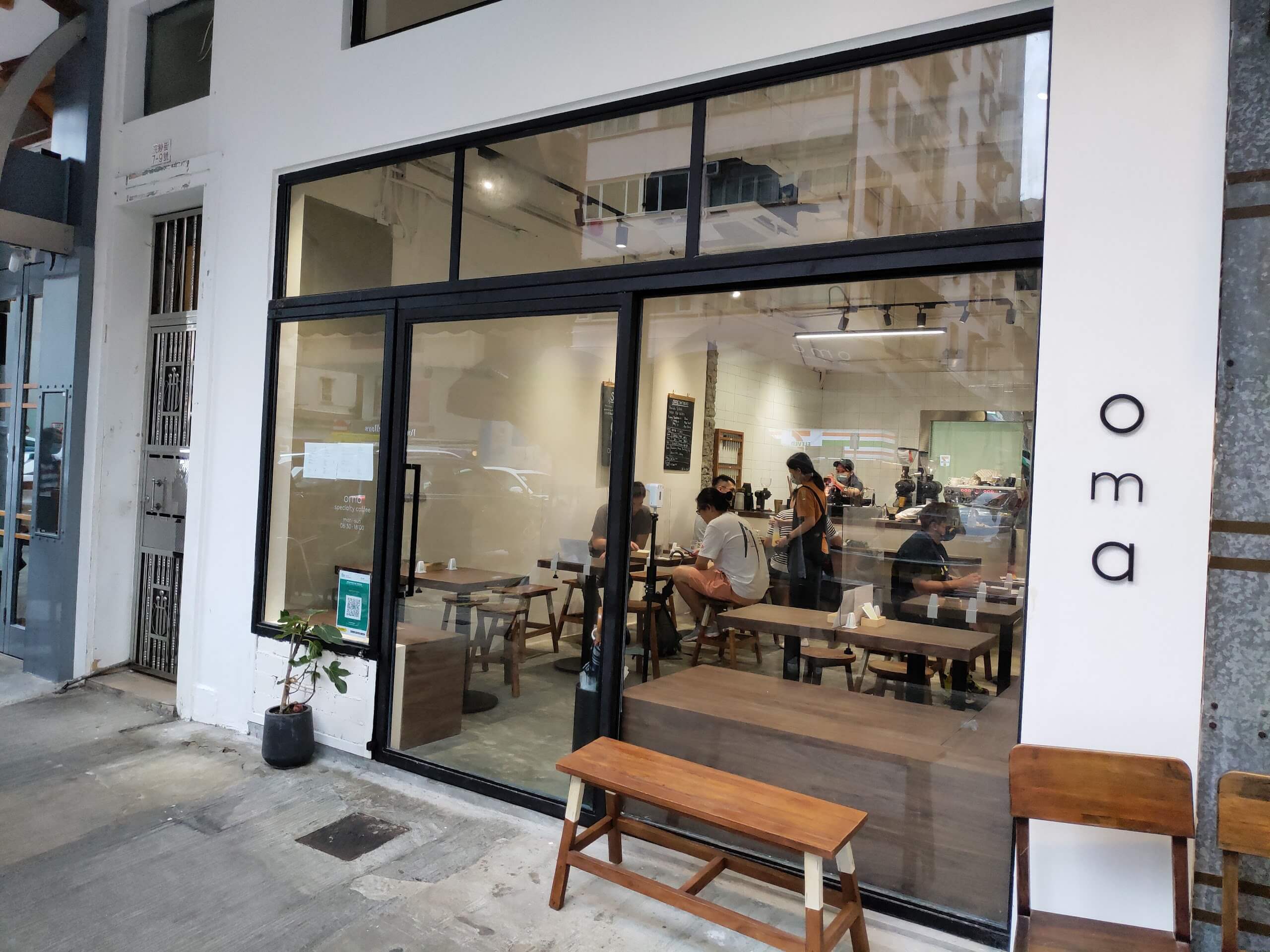 Oma’s white storefront, wooden benches and glass-fronted seating area on Wun Sha Street.
